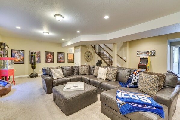 A spacious living room with a sectional sofa, ottoman, and a gaming arcade.