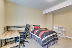A bedroom with a bed, desk, chair, and shelving unit.