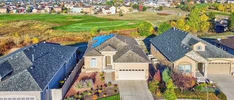 A residential area with houses featuring sloped roofs and solar panels, surrounded by a well-maintained lawn and a golf course in the background.