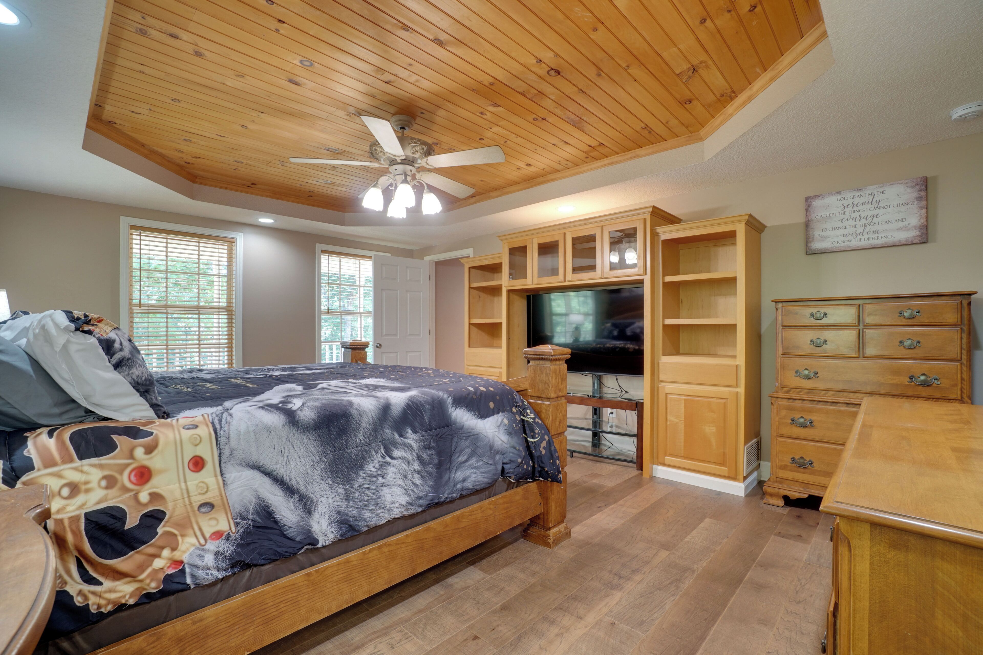 A bedroom with a bed, wooden ceiling, built-in TV, and wooden furniture.