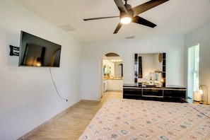 A bedroom with a bed, a ceiling fan, a TV mounted on the wall, a dresser, and a mirror. - On Preserved Land w/ Pool & Trails! Cape Coral Gem (Cape Coral)