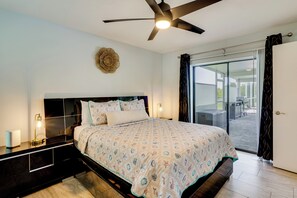 A bedroom with a bed, bedside lamps, a ceiling fan, a decorative wall piece, and a sliding glass door to an outdoor area. - On Preserved Land w/ Pool & Trails! Cape Coral Gem (Cape Coral)