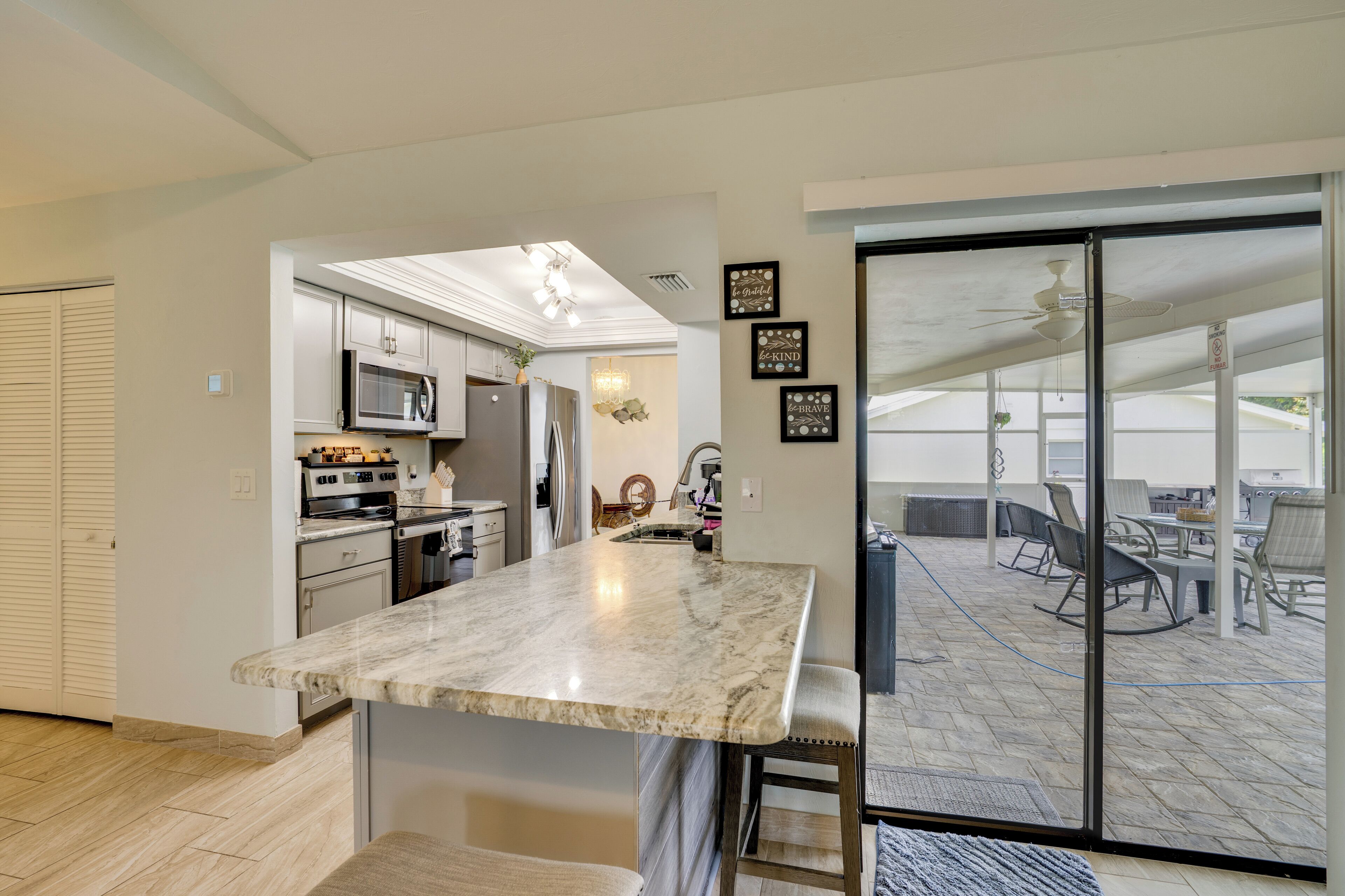 A modern kitchen with a marble countertop, stainless steel appliances, and a sliding glass door leading to an outdoor patio area.