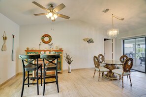 Un comedor con ventilador de techo, lámpara de araña, mesa redonda con sillas y un elemento decorativo en la pared.