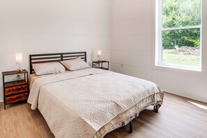 Ein Schlafzimmer mit Bett, Nachttischen, einem Fenster und Blick ins Grüne.