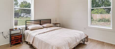 Un dormitorio con cama, mesitas de noche, lámpara, ventana y vista al exterior.