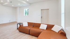 A spacious room with a brown leather sofa, a small black side table, and a window with a view of greenery. - Close to Ohio River: 6BR Jeffersonville Home (Jeffersonville)