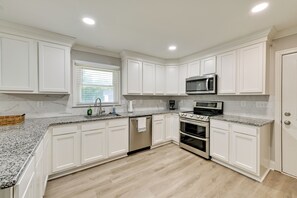 A modern kitchen with white cabinetry, granite countertops, a built-in microwave, a stove, and a dishwasher.