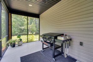A modern kitchen with a built-in grill, potted plants, and large windows offering a view of the forest. - 'The Romano Retreat' Modern Lake Guntersville Home (Scottsboro)