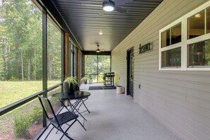 A covered porch with a table and chairs, large windows, and a view of the surrounding forest. - 'The Romano Retreat' Modern Lake Guntersville Home (Scottsboro)