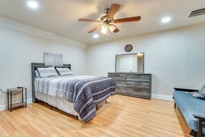 Ein Schlafzimmer mit Bett, Kommode, Stuhl, Deckenventilator und Wanduhr.