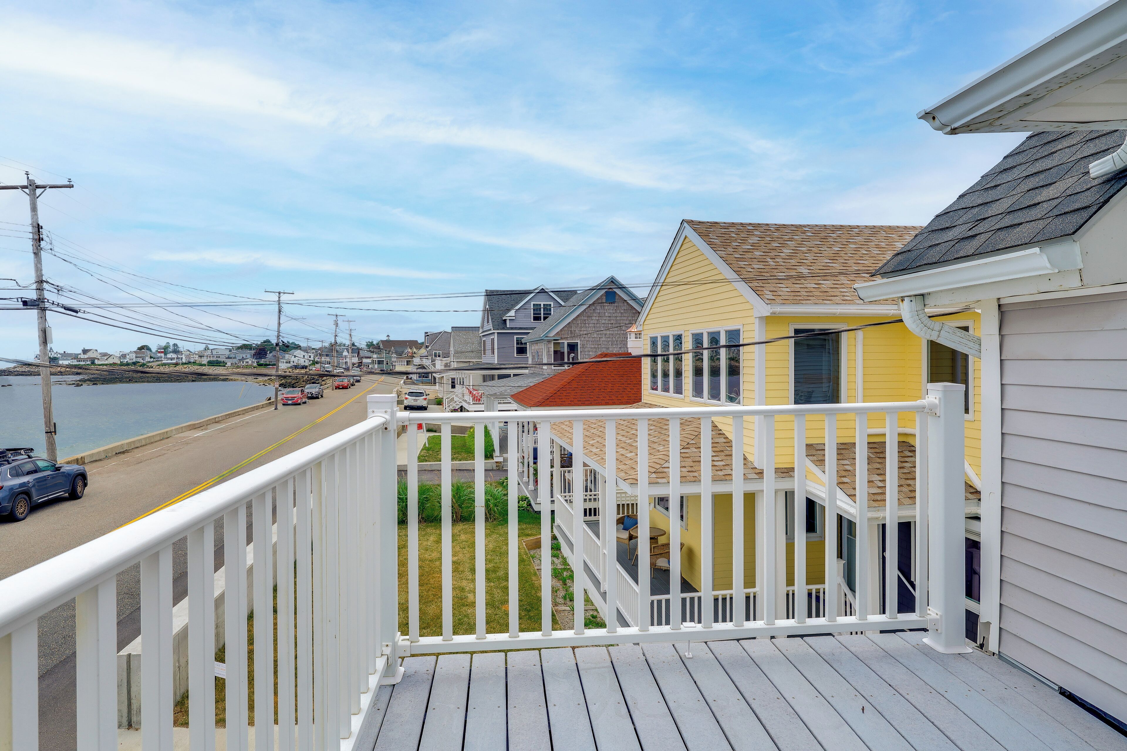 A balcony with a view of a coastal road, houses, and a body of water.