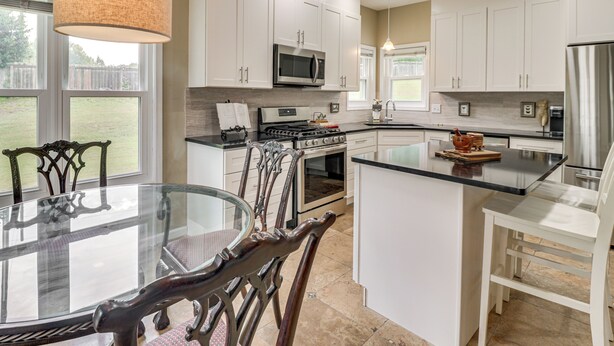 A modern kitchen with white cabinetry, a central island, and a dining area with a glass table and dark chairs. - 8 Mi to Marietta: Spacious Powder Springs Home (Powder Springs)