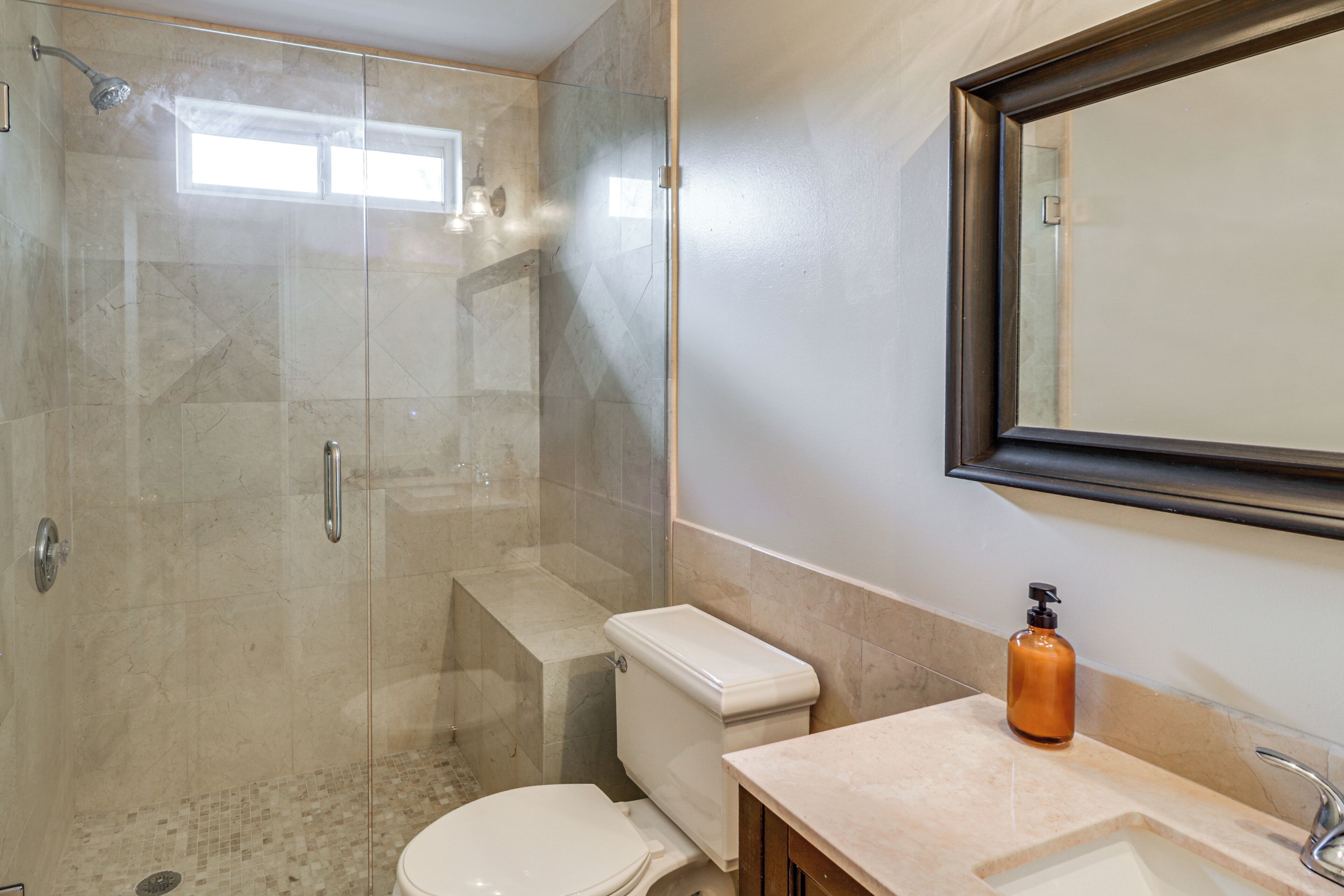 A bathroom with a glass-enclosed shower, a toilet, a sink, and a mirror.