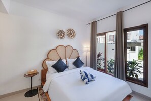 Habitación de hotel con una cama, una mesita, dos adornos en la pared y vistas al exterior.