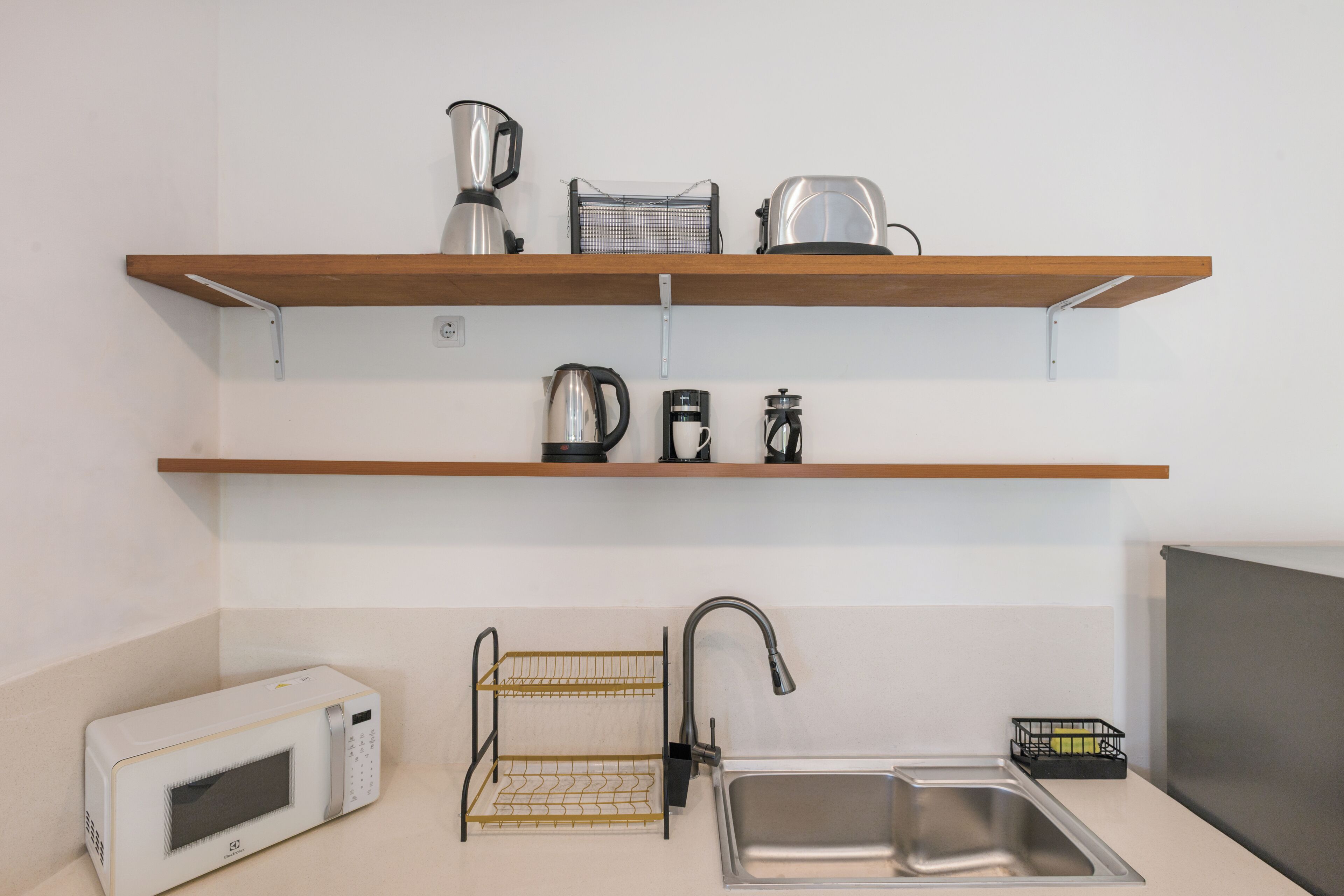 A kitchen with a microwave, a sink, a faucet, and two shelves with kitchen appliances.