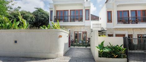 A residential building with a paved driveway, a gated entrance, and a small garden area.