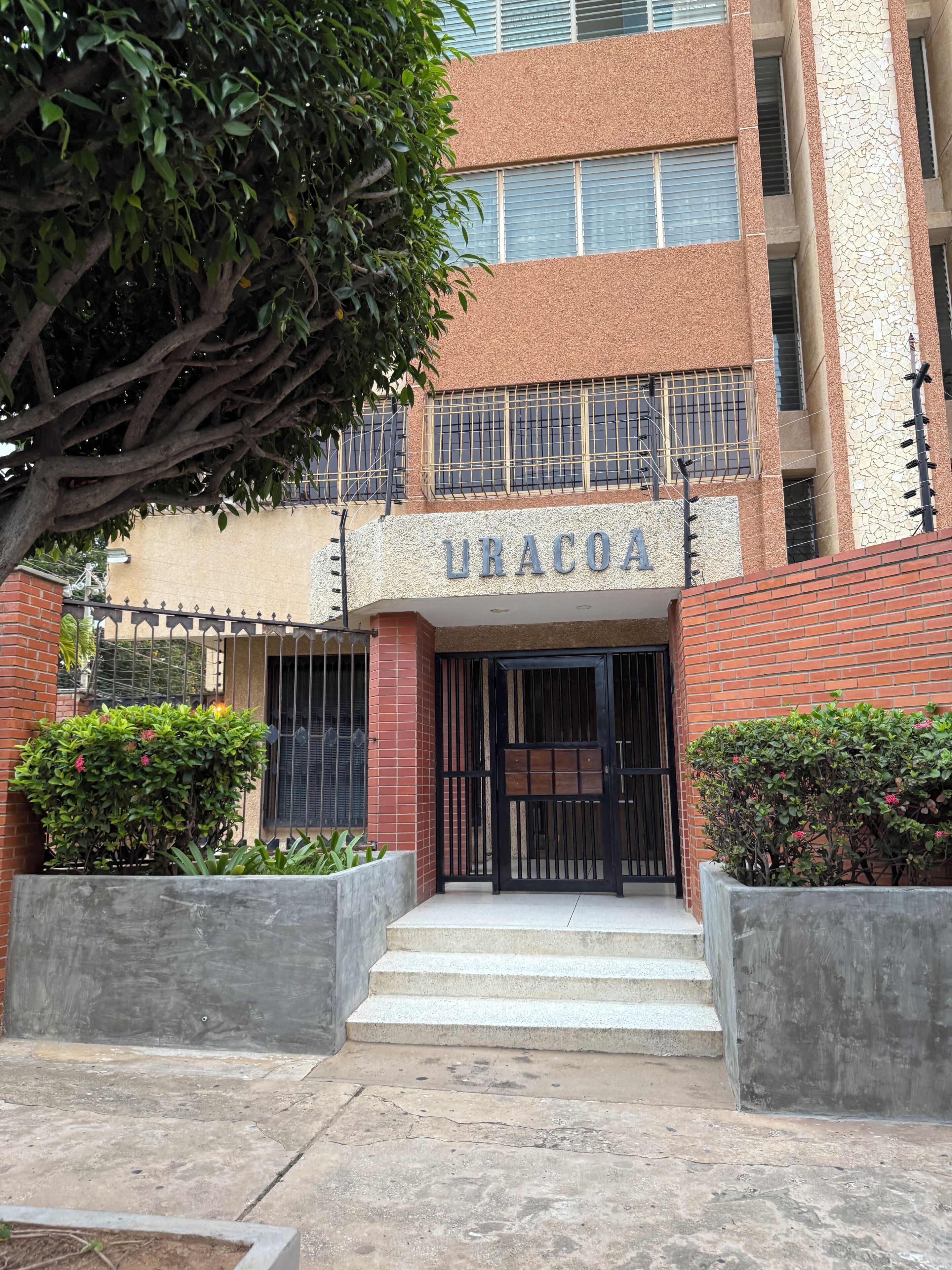 Edifici amb un rètol que diu 'URACOIA' a l'entrada, amb un portal tancat per reixa, una escala i façana de maó.