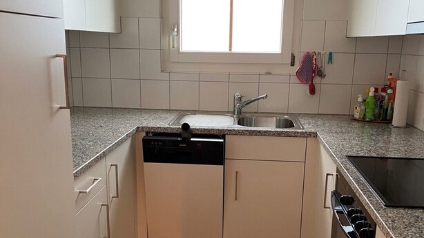 A compact kitchen with a built-in dishwasher, a sink, and a window above it.