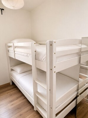 Una cama litera con un espejo a la derecha, ropa de cama blanca y suelo de madera.