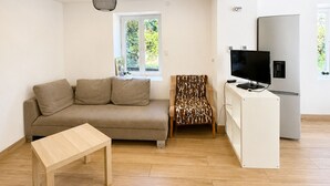 Ein modernes Wohnzimmer mit einer Couch, einem gemusterten Sessel, einem Fernseher und einem weißen Schrank.