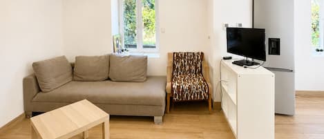 A modern living room with a sofa, a patterned armchair, a TV, and a white cabinet.