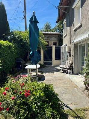 A courtyard with a table and chairs, a covered umbrella, and a stone building with a gate.