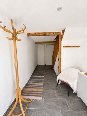A hallway with a coat rack, a striped rug, a white chair, and a wooden staircase.