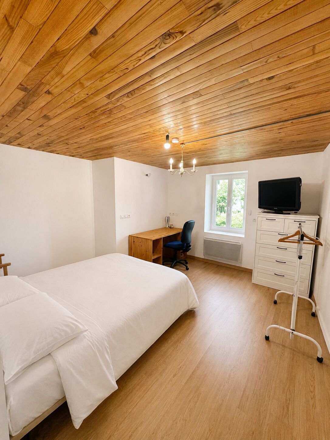 A bedroom with a wooden ceiling, a bed, a desk with a chair, a television, and a dresser.