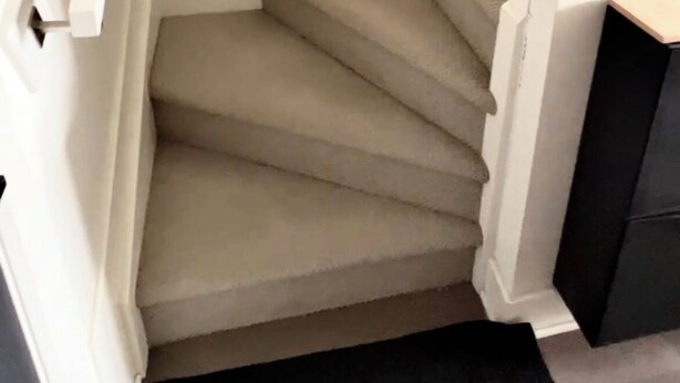 A staircase with a carpeted interior, white walls, and a small light fixture on the wall.