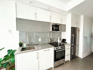 A modern kitchen with white cabinetry, a stainless steel refrigerator, a built-in oven, and a microwave.