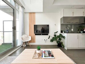 Ein modernes Wohnzimmer mit Flachbildfernseher, Couchtisch mit einer Zeitschrift, einer Zimmerpflanze und Blick ins Freie.