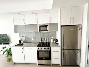 Eine moderne Küche mit weißen Schränken, einem Edelstahlkühlschrank, einem eingebauten Backofen und einer Mikrowelle.