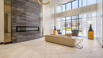A modern lobby with a large seating area, a reception desk, and large windows providing a view of the outside.