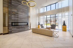 A modern lobby with a large seating area, a reception desk, and large windows providing a view of the outside.