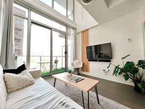 Ein modernes Wohnzimmer mit Sofa, Couchtisch, Fernseher und einem Balkon mit Blick auf Gebäude.
