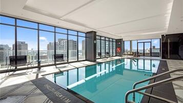 A modern indoor swimming pool with large windows and a city view.