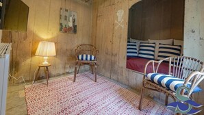 A rustic room with wooden walls, a bed with striped pillows, a wicker chair, a small stool with a lamp, and a patterned rug. - Spacious Coastal Home in Koudekerke (Koudekerke)