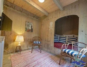A rustic room with wooden walls, a bed with striped pillows, a wicker chair, a small stool with a lamp, and a patterned rug. - Spacious Coastal Home in Koudekerke (Koudekerke)