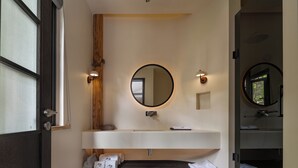 A bathroom with a large mirror, a white sink, and a dark wooden shelf with towels.