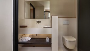 A modern bathroom with a built-in sink, a mirror, a toilet, and a shelf with towels.