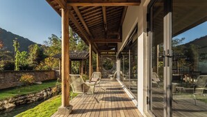 A covered outdoor seating area with wicker chairs, a stone wall, and a view of the surrounding landscape.