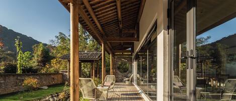 A covered outdoor seating area with wicker chairs, a stone wall, and a view of the surrounding landscape.