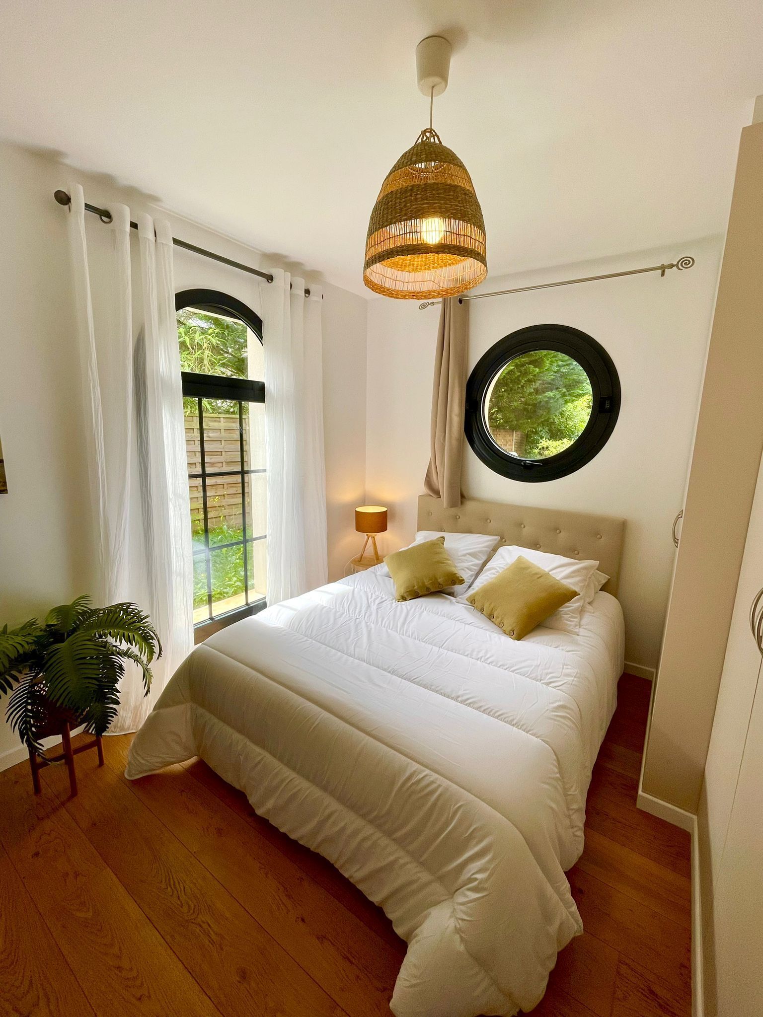 Un dormitorio con una cama grande, un ventanal redondo y una lámpara colgante.