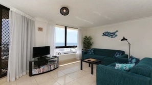 A living room with a TV, a sofa, a coffee table, and a view of the sea. - Palm Beach Stunning Ocean Apartment! (Palm Beach)
