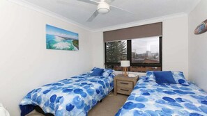 A bedroom with two beds, a ceiling fan, a window with a view, and a painting on the wall. - Palm Beach Stunning Ocean Apartment! (Palm Beach)