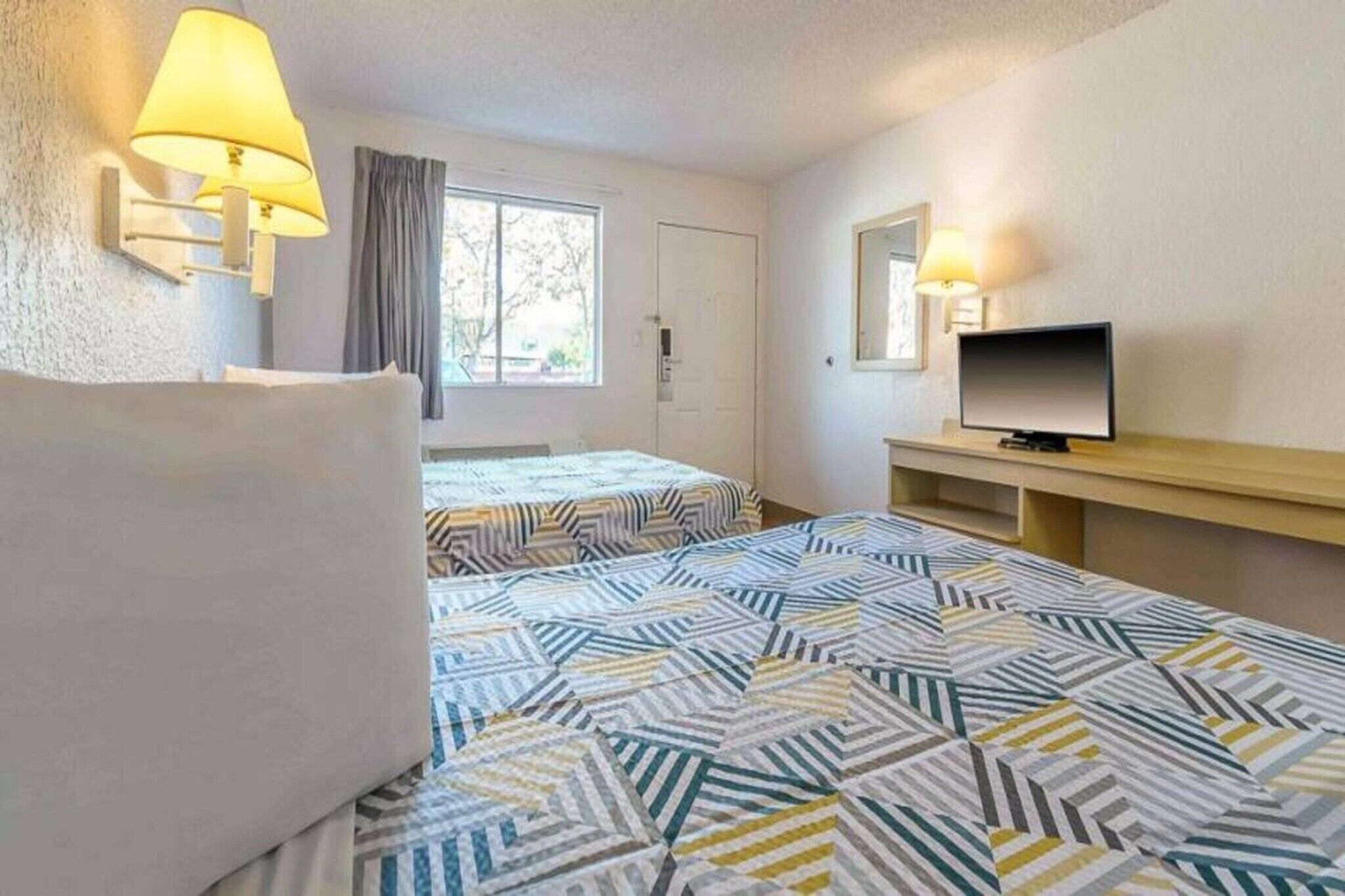 A hotel room with two beds, a television, and a window with curtains.