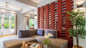 Un salon moderne avec un canapé d’angle, une table basse ronde agrémentée de livres et de bougies, une plante décorative et un mur en briques rouges avec une fenêtre.