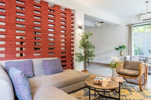 A modern living room with a sectional sofa, a round coffee table, a wicker chair, and a potted plant. - Staymaster Trivala-3BR Villa with Pool  (Calangute)
