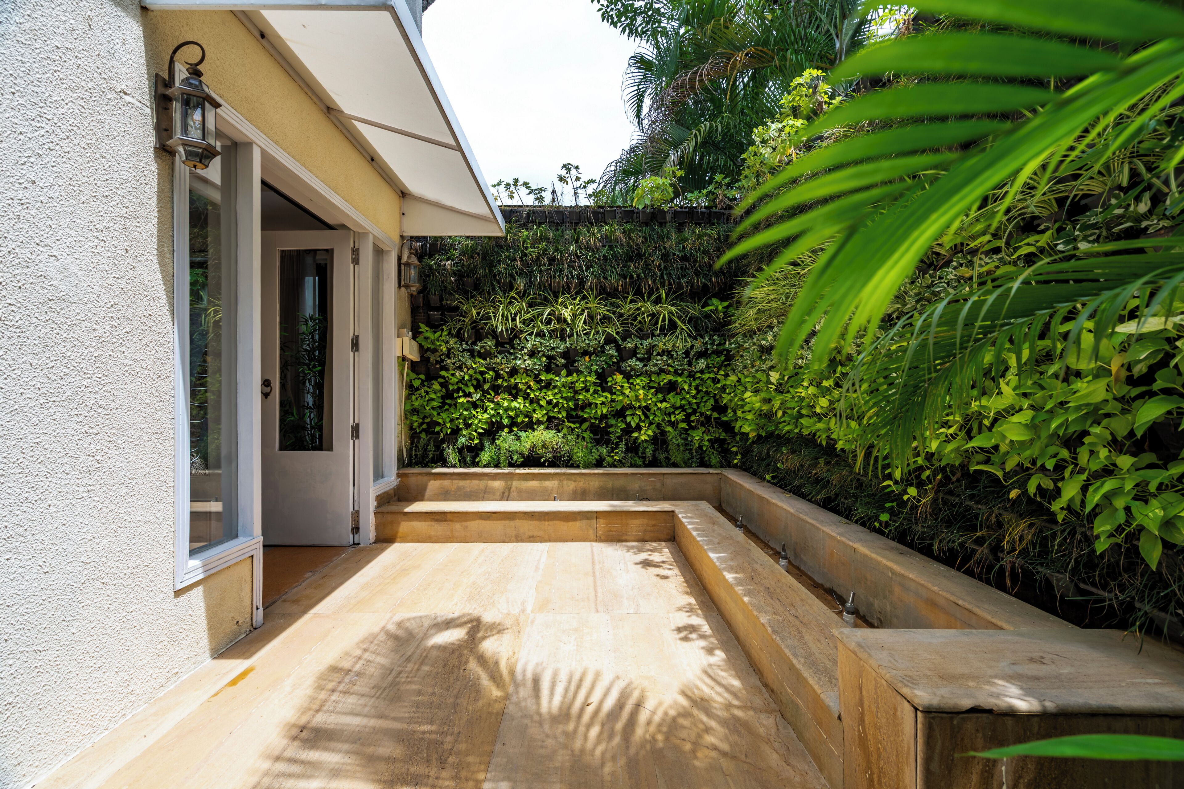 Eine Terrasse mit Holzboden, weißer Wand und einer grünen Hecke.